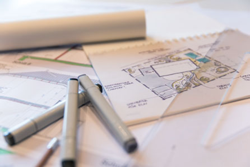 Nahaufnahme von Architekturplänen, Skizzen und Zeichentools wie Stiften und Transparentlineal.