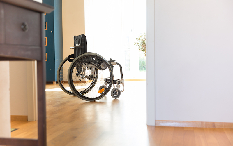 Leer stehender Rollstuhl in einem hellen Wohnraum mit Holzfußboden.