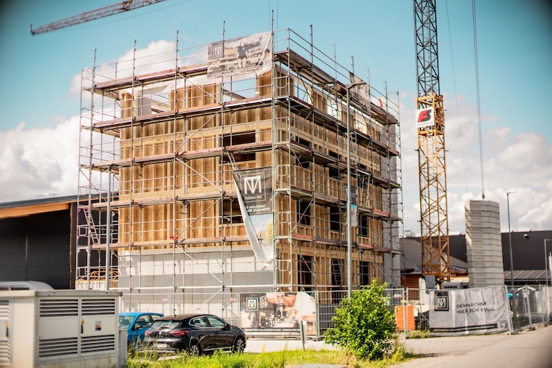 Mehrgeschossiges Holzgebäude im Rohbau, eingerüstet und mit Kran auf einer modernen Baustelle.